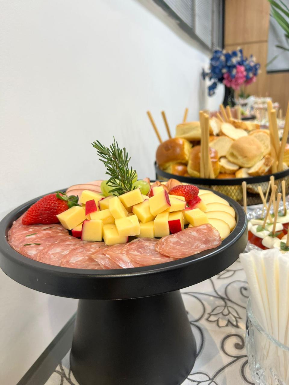 Tábua de frios em pedestal preto com salame, queijos e morangos
